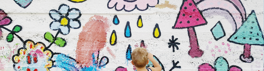 Kid creating a mural, with white backdrop and whimsical design